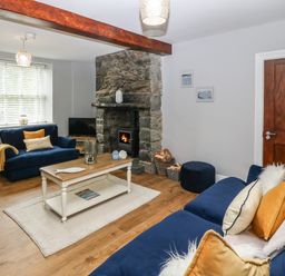 A living room with blue sofas a stone fireplace wooden coffee table and a wooden door at Belle View in Llaniestyn near Abersoch