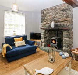 A living room with a stone fireplace a blue sofa a wooden coffee table and firewood at Belle View in Llaniestyn near Abersoch