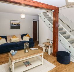 A living room with a blue sofa pillows a wooden coffee table a staircase with glass balustrade and a wooden pillar at Belle View in Llaniestyn near Abersoch