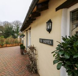The exterior wall of a building with a sign reading The Shippen a paved walkway and plants in pots near the building at The Shippen in Gooseham near Kilkhampton