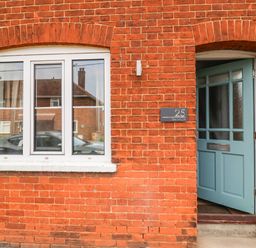 A brick exterior wall with a white framed window and a partially open blue door at Sea Mouse Cottage in Southwold