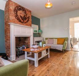 A living room with a brick fireplace a wooden coffee table two green sofas and a lamp at Sea Mouse Cottage in Southwold