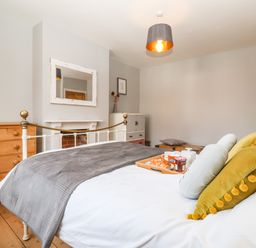 A bedroom with a bed and breakfast tray next to a wooden dresser and a mirror above a fireplace at Sea Mouse Cottage Southwold
