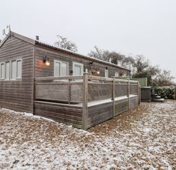 A wooden cabin with a fenced deck and snow on the ground at Grouse Lodge in Seamer North Yorkshire