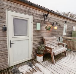 An outdoor wooden deck with a bench plant pots hanging basket and a white door at Grouse Lodge in Seamer North Yorkshire