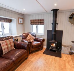 A living room with leather sofa and armchair near a wood burning stove and large wall clock at Grouse Lodge Seamer North Yorkshire