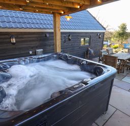 An outdoor hot tub with bubbling water on a patio next to a wooden dining table and chairs at Foxes Den in Seamer North Yorkshire