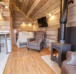 A small wooden room with a bed a leather armchair a wood burning stove and a wall mounted TV at Sunset Retreat in Seamer North Yorkshire