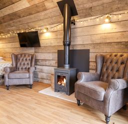 A room with two armchairs a wood stove a wall mounted tv and a bed at Sunset Retreat in Seamer North Yorkshire