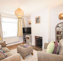 A living room with two sofas a cushioned ottoman a television and a fireplace at Quarrier's Rest in Swanage