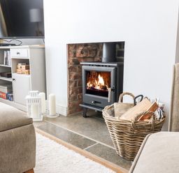 A living room area with a wood-burning stove and basket of firewood next to a television cabinet at Quarrier's Rest in Swanage