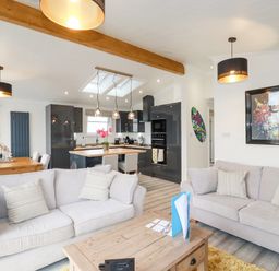 An open living room and kitchen with sofas coffee table dining table and modern cabinets at Mordros Lodge in St Day