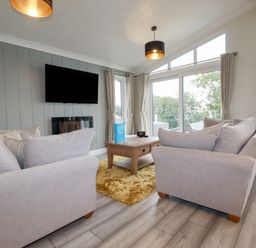 A living room with two sofas a wooden coffee table a wall-mounted television and large windows at Mordros Lodge in St Day