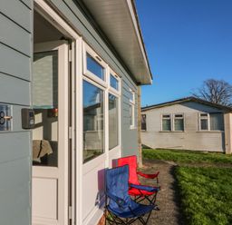 Front exterior of a holiday chalet with two folding chairs on a path by the door at Beachcomber Norton Park near Dartmouth