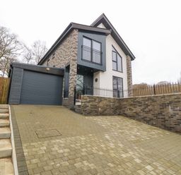A modern two-story house with a brick and plaster exterior and a closed garage door with driveway and steps at Ty Bains in Llanberis