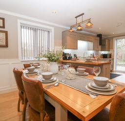 A dining area with a wooden table set with bowls plates glasses and cutlery with leather chairs and a kitchen in the background at Ty Bains in Llanberis