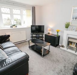 A living room with black leather sofas a glass coffee table a television on a stand and a fireplace at 17 Ffordd Gwenllian in Llanfairpwllgwyngyll
