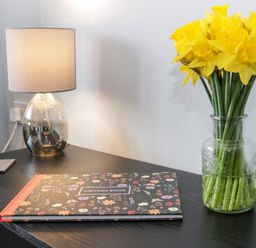 A table with a lamp visitors book and a glass vase with yellow flowers at 17 Ffordd Gwenllian in Llanfairpwllgwyngyll