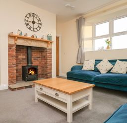 A living room with a fireplace a wooden coffee table and blue sofas at Garden Cottage in Alnmouth