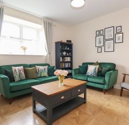 A living room with two green sofas a wooden coffee table a gray armchair and a bookshelf at Pond Cottage in Alnmouth