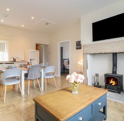 An open kitchen and dining area with a table set for four and a wood burning stove with TV above at Pond Cottage in Alnmouth