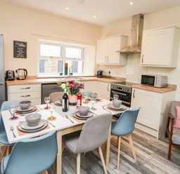 A kitchen and dining area with a dining table set for six and modern appliances at Lonnon Cottage in Alnmouth