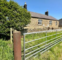 A stone house with two chimneys behind a metal gate and grassy area at Lonnon Cottage in Alnmouth