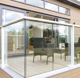 A patio with glass railing and outdoor chairs and a table with wine glasses at Willow Lodge in Winthorpe near Newark-On-Trent