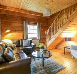 A living room with a leather sofa a round glass coffee table a gray armchair and wooden stairs at Moyle Lodge in Dalbeattie