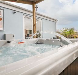 An outdoor hot tub with water jets near a light blue house with windows and a sliding door at The View in Cardinham