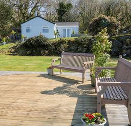 An outdoor deck with two wooden benches and potted plants overlooking a grassy lawn with a white house and trees at The View in Cardinham