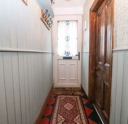 A narrow hallway with a red patterned runner rug a wooden door on the right and a white door with stained glass at the end at Bod Feurig in Penygroes