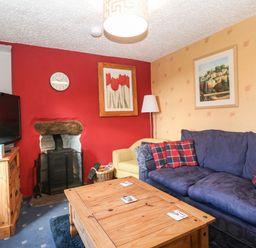 A living room with a blue sofa a wooden coffee table a TV on a wooden stand and a fireplace at Bod Feurig in Penygroes