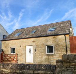 A stone cottage with a white door and two small windows behind a stone wall at Stable Cottage in Hallbankgate