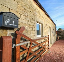 A stone exterior wall with a black mailbox numbered 6 and a wooden gate at Stable Cottage in Hallbankgate