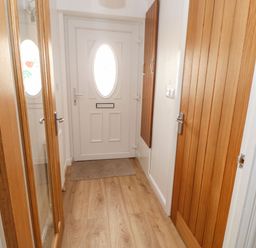 A hallway with a white door with an oval window a wooden floor a carpet a wooden door and a tall mirror at Stable Cottage in Hallbankgate