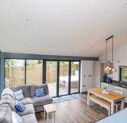 An open plan living room and kitchen with gray sofa, wooden dining table, and sliding glass doors at The Nest Brython in Tenby