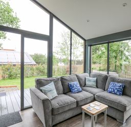 A sitting area with a gray L-shaped sofa and small wooden table in a room with large glass windows and doors at The Nest Brython in Tenby