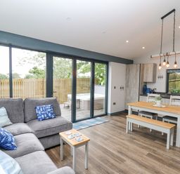An open plan living room and kitchen with a grey sofa and wooden dining table at The Nest Brython in Tenby