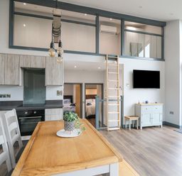 A kitchen and dining area with wooden table and chairs loft ladder and wall mounted tv at Cornerstones Brython in Tenby