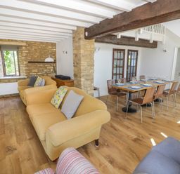 A living room with yellow sofas and a dining table set with plates and glasses at The Paddock in New Yatt near Witney