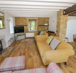A living room with yellow sofas a striped armchair a television and stone walls at The Paddock in New Yatt near Witney