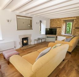 A living room with two yellow sofas a striped armchair a fireplace a wall mirror a television and two windows at The Paddock in New Yatt near Witney