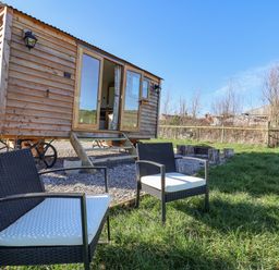 A small wooden caravan with steps and two black chairs with white cushions on grass at Cariad Bach in Gwaenysgor near Prestatyn