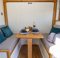 A small dining area with wooden table and cushioned bench seats with pillows at Cariad Bach in Gwaenysgor near Prestatyn