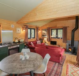 A living area with a round dining table and chairs a kitchen with green cabinets and a stove and a sitting area with red sofas a wood burning stove and windows with curtains at Willow in Dunchurch