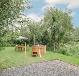 An outdoor garden with a wooden hot tub table with umbrella chairs and trees at Dragonfly in Dunchurch