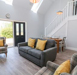 A living area with a gray sofa and two plaid armchairs with yellow cushions a wooden dining table with chairs under stairs at Willow Cottage in Combe Martin