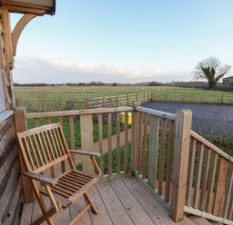 A wooden chair on a small wooden balcony overlooking a field with grazing sheep at Arts and Crafts in Bolton Percy near Tadcaster