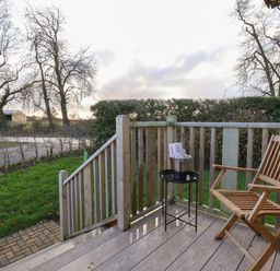 A wooden deck with a chair and a small table with a bucket on it overlooking a garden at Arts and Crafts in Bolton Percy near Tadcaster